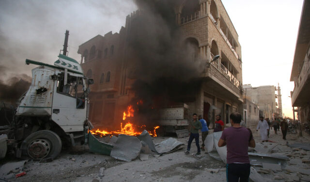 EDITORS NOTE: Graphic content / People walk amidst rubble as part of a building burns following a reported airstrike by Syrian regime forces in  Maaret al-Numan in Syria's northwestern Idlib province on August 28, 2019. (Photo by Abdulazez Ketaz / AFP)