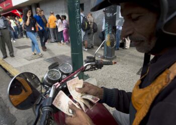 A man counts 100 Bolivar notes in the street whilst people queue outside a bank in Caracas in an attempt to deposit money, on December 15, 2016.
According to the UN's Economic Commission for Latin America and the Caribbean (ECLAC) forecast, Venezuela's economy will shrink 9.7 percent this year. / AFP PHOTO / FEDERICO PARRA