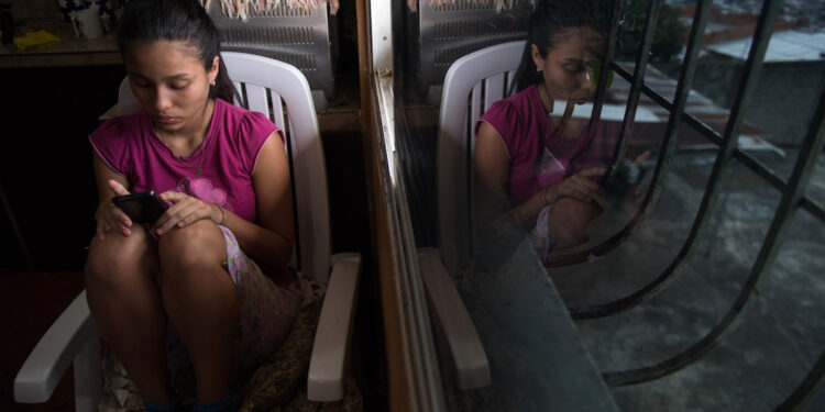 Venezuelan Dougliannys Perez, 15, whose parents emigrated, uses her cellphone after an interview with AFP, at Petare neighborhood in Caracas on August 9, 2019. - The crisis in Venezuela has broken up families since parents migrate to pay for the living of the children they leave behind. Some 850,000 children live without their parents in the country according to the NGO Cecodap. (Photo by Federico PARRA / AFP)