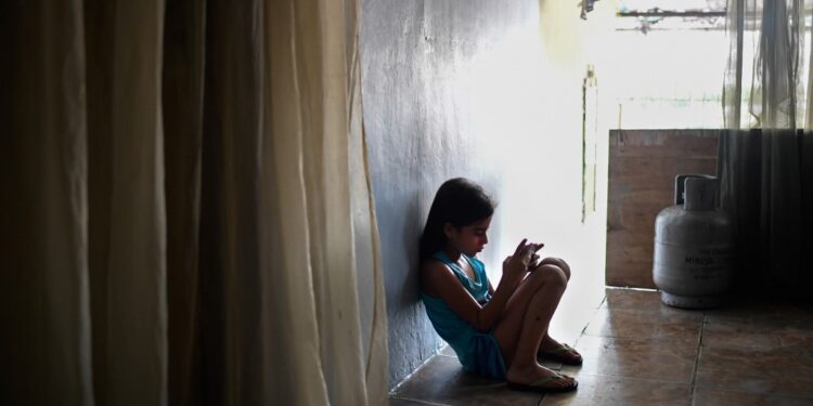 Venezuelan Paola Osorio, 7, whose parents emigrated, uses a cell phone at her house of the San Agustin neighborhood in Caracas on August 5, 2019. - The crisis in Venezuela has broken up families since parents migrate to pay for the living of the children they leave behind. Some 850,000 children live without their parents in the country according to the NGO Cecodap. (Photo by Federico PARRA / AFP)