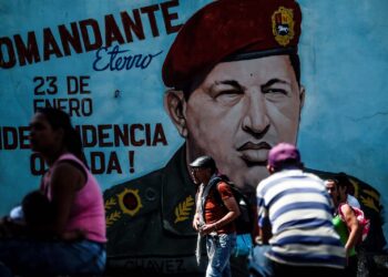 People walk past a painting of late Venezuelan President Hugo Chavez on a wall in Caracas on January 29, 2019. - Venezuelan President Nicolas Maduro moved Tuesday to try to check the growing clout of opposition rival Juan Guaido as the United States tightened its stranglehold on the leftist regime's main source of revenues. (Photo by Juan BARRETO / AFP)