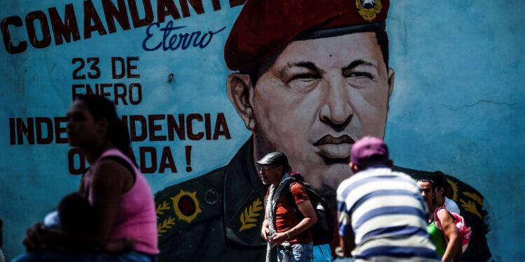 People walk past a painting of late Venezuelan President Hugo Chavez on a wall in Caracas on January 29, 2019. - Venezuelan President Nicolas Maduro moved Tuesday to try to check the growing clout of opposition rival Juan Guaido as the United States tightened its stranglehold on the leftist regime's main source of revenues. (Photo by Juan BARRETO / AFP)