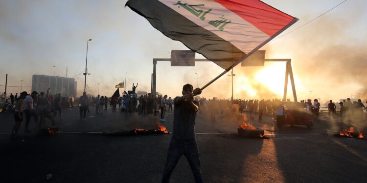 TOPSHOT - An Iraqi protester waves the national flag during a demonstration against state corruption, failing public services, and unemployment, in the Iraqi capital Baghdad on October 5, 2019. Renewed protests took place under live fire in Iraq's capital and the country's south Saturday as the government struggled to agree a response to days of rallies that have left nearly 100 dead. The largely spontaneous gatherings of demonstrators -- whose demands have evolved since they began on Tuesday from employment and better services to fundamental government change -- have swelled despite an internet blackout and overtures by the country's elite. Hours after a curfew in Baghdad was lifted on Saturday morning, dozens of protesters rallied around the oil ministry in the capital, facing live rounds fired in their direction, an AFP photographer said. / AFP / AHMAD AL-RUBAYE