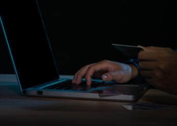 Cyber crime concept: Anonymous man holding credit card with laptop on his hand