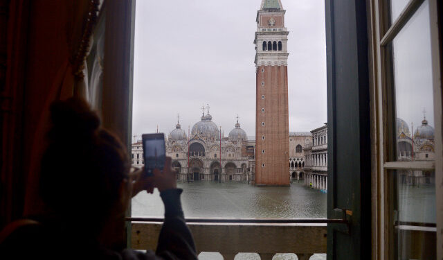 A woman takes a photo of the flooded St. Mark's Square, with St. Mark's Basilica (Rear) and the Bell Tower on November 15, 2019 in Venice, two days after the city suffered its highest tide in 50 years. - Flood-hit Venice was bracing for another exceptional high tide on November 15, as Italy declared a state of emergency for the UNESCO city where perilous deluges have caused millions of euros worth of damage. (Photo by Filippo MONTEFORTE / AFP)