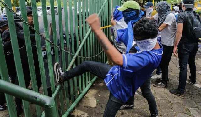 An anti-government protester kicks a riot police shield during a protest of students and relatives of political prisoners in front of a police line at the Universidad Centroamericana (UCA) in Managua on November 19, 2019. - Last week about 16 people were arrested and prosecuted for bringing water to mothers of political prisoners who were going on a hunger strike in Masaya. (Photo by INTI OCON / AFP)