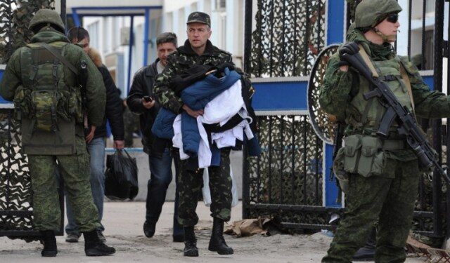 Ukrainian officers leave as Russian soldiers stand guard at the Ukrainian navy headquarters in the Crimean city of Sevastopol on March 19, 2014.  Ukrainian servicemen filed out of navy headquarters in Sevastopol on Wednesday with tears in their eyes after the base was seized by pro-Moscow militants, Russian troops and Cossack forces.  The assault began when some 200 unarmed militants -- some of them in balaclavas -- sawed through a fence and overran the base while the Ukrainian servicemen barricaded themselves inside.  AFP PHOTO/  VIKTOR DRACHEV