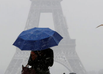 A woman holds an umbrella to protect herself from falling snow near the Eiffel Tower in Paris, as winter weather with snow and freezing temperatures arrive in France, February 6, 2018. REUTERS/Gonzalo Fuentes - RC12AF5ABA60