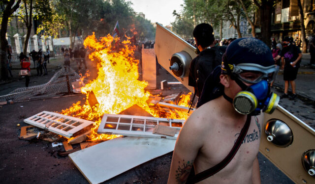 Demonstrators throw objects into a bonfire during clashes with riot police as they protest against the government, in Santiago, on December 06, 2019. - Thusands protested in Santiago Friday after 50 days of social crisis -the worst in 30 years-, which has downturned local economy. (Photo by Martin BERNETTI / AFP)
