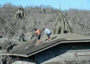 Dos hombres limpian el techo de su vivienda, cubierto de barro y cenizas por la erupción del cercano volcán Taal, el 16 de enero de 2020 en el pueblo de Laurel, en Filipinas© AFP Ted Aljibe