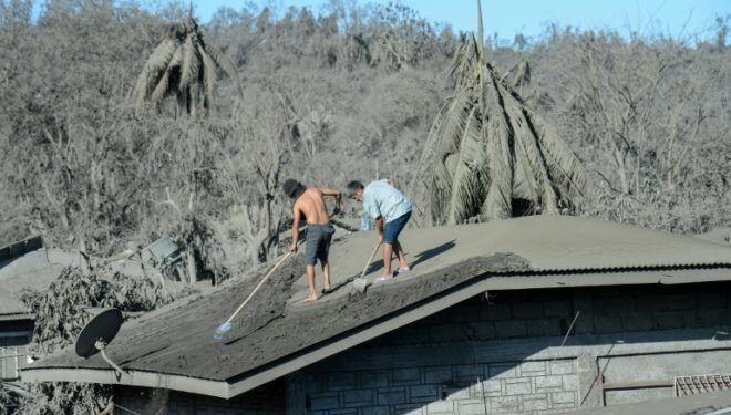 Dos hombres limpian el techo de su vivienda, cubierto de barro y cenizas por la erupción del cercano volcán Taal, el 16 de enero de 2020 en el pueblo de Laurel, en Filipinas© AFP Ted Aljibe