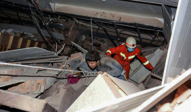 A man (L) is helped by rescuers as he is pulled from the rubble of a collapsed hotel in Quanzhou, in China's eastern Fujian province on March 7, 2020. - Around 70 people were trapped after the Xinjia Hotel collapsed on March 7 evening, officials said. (Photo by STR / AFP) / China OUT