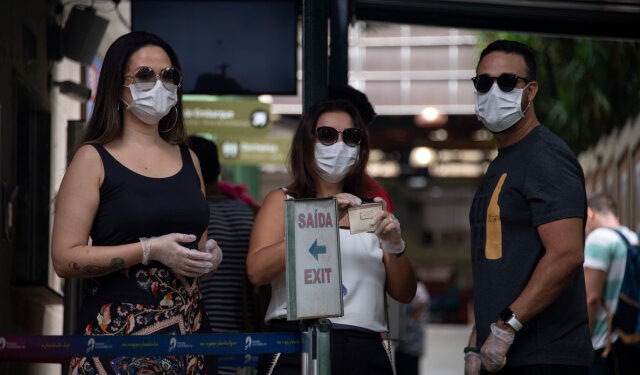 Tourists wears face masks after buying tickets at the Corcovado hill train station, to go up to see the statue of Christ the Redeemer in Rio de Janeiro, Brazil, on March 17, 2020. - Rio de Janeiro's state government closed the iconic Christ the Redeemer statue and the cable car to Sugarloaf Mountain, two of the city's most famous attractions, as an emergency measure to stop the spread of the new coronavirus COVID-19. (Photo by MAURO PIMENTEL / AFP)