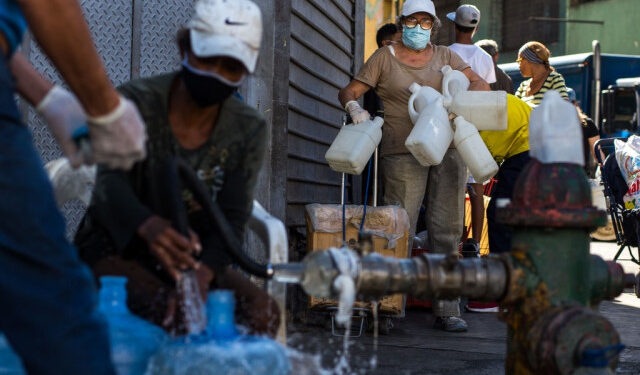 People wear face masks as a preventive measure against the global COVID-19 coronavirus pandemic as they wait to collect water from a street pipe in Caracas, on March 27, 2020. - Venezuela is facing the novel coronavirus pandemic while suffering a major gasoline shortage and with the country's water system collapsed, which has left many homes without running water. (Photo by Cristian Hernandez / AFP)