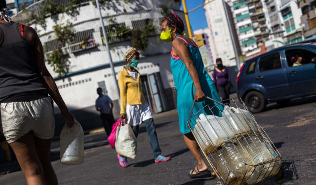 People wear face masks as a preventive measure against the global COVID-19 coronavirus pandemic as they carry water cans collected from a street pipe in Caracas, on March 27, 2020. - Venezuela is facing the novel coronavirus pandemic while suffering a major gasoline shortage and with the country's water system collapsed, which has left many homes without running water. (Photo by Cristian Hernandez / AFP)