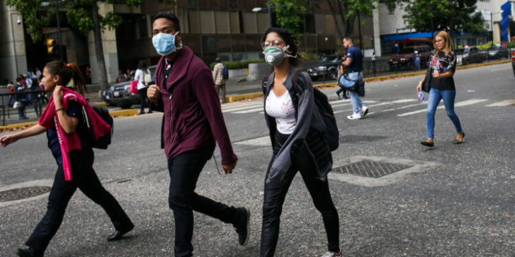 People wearing face masks walk in the street in the face of the global COVID-19 coronavirus pandemic, in Caracas, on March 13, 2020. (Photo by CRISTIAN HERNANDEZ / AFP)