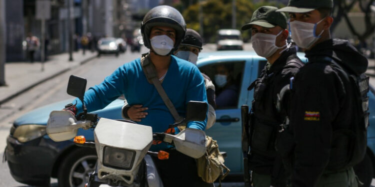 Members of the Bolivarian National Guard (R) block an avenue wearing face masks as a precautionary measure against the spread of the new coronavirus, COVID-19, in Caracas, on March 17, 2020 - President Nicolas Maduro asked the International Monetary Fund on Tuesday for a $5 billion loan to help crisis-worn Venezuela cope with the onslaught of the coronavirus. (Photo by Cristian Hernandez / AFP)