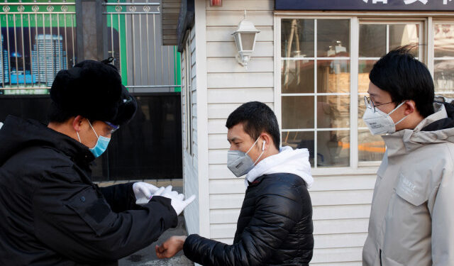 Un guardia de seguridad toma la temperatura de personas que llegan a trabajar a un edificio de oficinas en Pekín, China, 3 de marzo de 2020. REUTERS/Thomas Peter