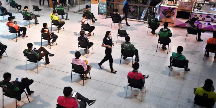 Food delivery drivers and customers sit on chairs spaced apart for social distancing, as part of the effort to contain the COVID-19 coronavirus, as they wait for takeaway orders at Central Pinklao shopping mall in Bangkok on March 26, 2020. (Photo by Lillian SUWANRUMPHA / AFP)