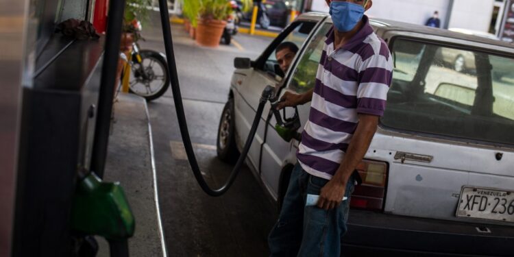 A man fills a car with gasoline at a gas station wearing a face mask as a precautionary measure against the spread of the new coronavirus, COVID-19, in Caracas on March 23, 2020. - Venezuela is facing the novel coronavirus pandemic while suffering a major gasoline shortage and with the country's water system collapsed, which has left many homes without running water. (Photo by Cristian Hernandez / AFP)