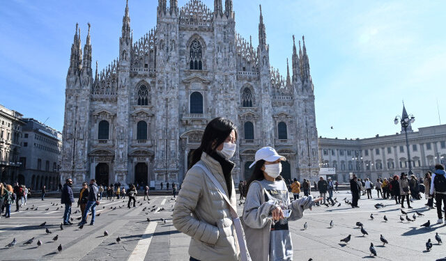 Two women wearing a protective facemask walk across the Piazza del Duomo, in front of the Duomo, in central Milan, on February 24, 2020 closed following security measures taken in northern Italy against the COVID-19 the novel coronavirus. - Italy reported on February 24, 2020 its fourth death from the new coronavirus, an 84-year old man in the northern Lombardy region, as the number of people contracting the virus continued to mount. (Photo by ANDREAS SOLARO / AFP)