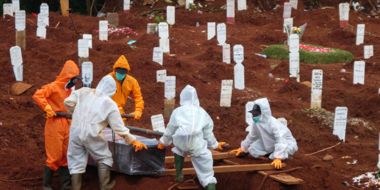 Workers move a coffin of a victim of the COVID-19 coronavirus to a burial site at a cemetery in Jakarta on April 15, 2020. (Photo by BAY ISMOYO / AFP)
