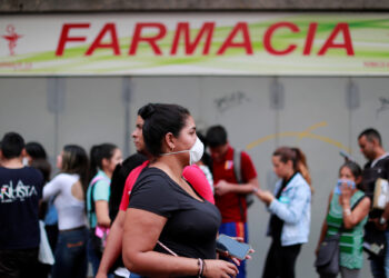 A woman wears a protective mask while people queue outside the pharmacy in response to coronavirus (COVID-19) spread, in Caracas, Venezuela March 13, 2020. REUTERS/Carlos Jasso