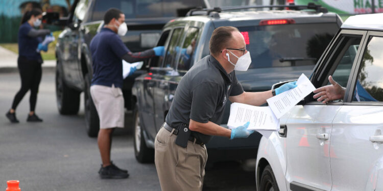 HIALEAH, FLORIDA - APRIL 08: Eddie Rodriguez (R) and other City of Hialeah employees hand out unemployment applications to people in their vehicles in front of the John F. Kennedy Library on April 08, 2020 in Hialeah, Florida. The city is distributing the printed unemployment forms to residents as people continue to have issues with access to the state of Florida’s unemployment website in the midst of widespread layoffs due to businesses closing during the coronavirus pandemic. (Photo by Joe Raedle/Getty Images)