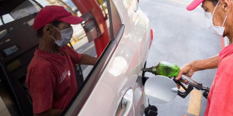A worker of a gas station fills the tank of a car with gasoline wearing a face mask as a precautionary measure against the spread of the new coronavirus, COVID-19, in Caracas on March 23, 2020. - Venezuela is facing the novel coronavirus pandemic while suffering a major gasoline shortage and with the country's water system collapsed, which has left many homes without running water. (Photo by Cristian Hernandez / AFP)