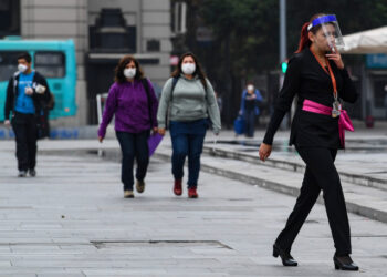 Pedestrians wear face masks as a precautionary measure against the spread of the new coronavirus, COVID-19, in Santiago, Chile, march 27, 2020. - More than 1.3 million people of seven of the main communes of Santiago will enter into total quarantine for a week starting Thursday night, after prolonging the suspension of classes due to the coronavirus epidemic that has left 1,610 confirmed cases and four deceased. (Photo by MARTIN BERNETTI / AFP)