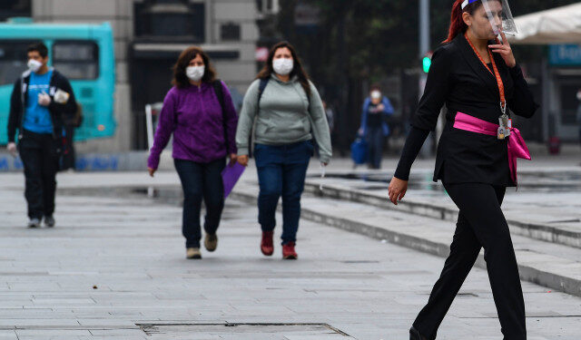 Pedestrians wear face masks as a precautionary measure against the spread of the new coronavirus, COVID-19, in Santiago, Chile, march 27, 2020. - More than 1.3 million people of seven of the main communes of Santiago will enter into total quarantine for a week starting Thursday night, after prolonging the suspension of classes due to the coronavirus epidemic that has left 1,610 confirmed cases and four deceased. (Photo by MARTIN BERNETTI / AFP)