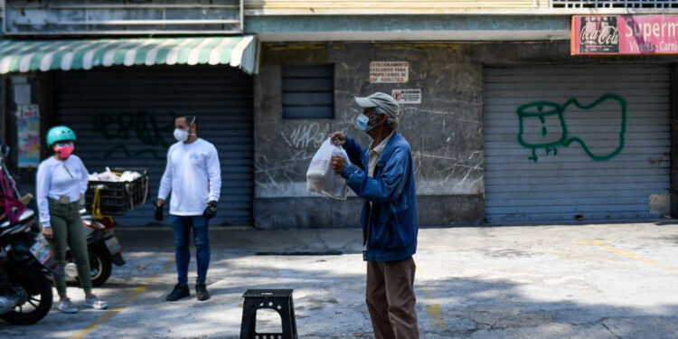 Volunteers deliver a meal bag to an elderly man as part of the "Good Neighbor Plan", in Caracas on April 28, 2020, amid the lockdown aimed at stopping the spread of the novel coronavirus. - The "Good Neighbor Plan" is an initiative started amid the new coronavirus pandemic to help elderly people without children or whose children have emigrated due to the crisis that has pushed 4,9 million Venezuelans out of the country since the end of 2015, according to the UN. (Photo by Federico PARRA / AFP)