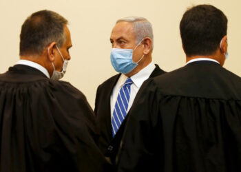 Israeli Prime Minister Benjamin Netanyahu (C), wearing a protective face maks, is pictured inside a courtroom at the district court of Jerusalem on May 24, 2020, during the first day of his corruption trial. - Fresh from forming a new government after more than 500 days of electoral deadlock, Netanyahu is expected to begin a new battle in the Jerusalem District Court -- to stay out of prison. The 70-year-old was scheduled to appear at a court hearing to formally confirm his identity to judges, after being indicted in January for bribery, fraud and breach of trust. (Photo by RONEN ZVULUN / POOL / AFP)