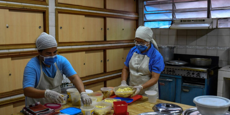 Religious sisters Teresa Gomez (R) and Analia pack meals prepared at the Inmaculada Nina de Santa Ana kindergarten, at Casalta neighborhood in Caracas on May 22, 2020, amid the lockdown aimed at stopping the spread of the novel coronavirus. (Photo by Federico PARRA / AFP)