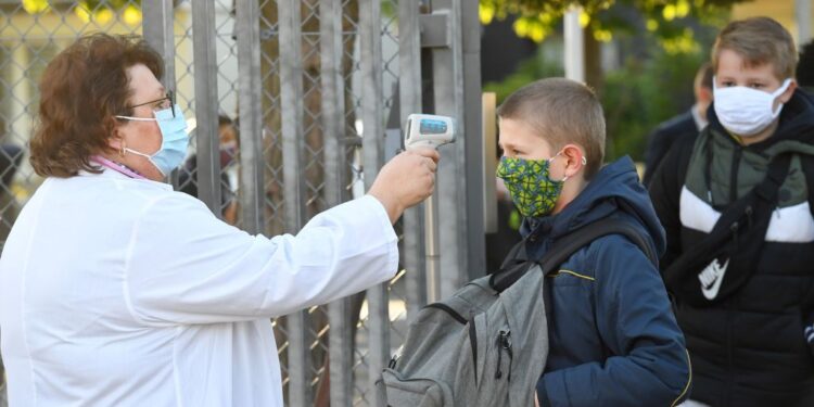 A member of the educational team checks body temperature of a schoolboy wearing a protective face mask before entering Claude Debussy college in Angers, western France, on May 18, 2020 after France eased lockdown measures to curb the spread of the COVID-19 pandemic, caused by the novel coronavirus. (Photo by Damien MEYER / AFP) (Photo by DAMIEN MEYER/AFP via Getty Images)