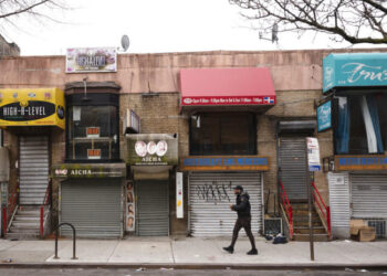 Fotografía de archivo del 8 de abril de 2020 de un peatón caminando frente a pequeños negocios que debieron cerrar sus puertas por la pandemia de coronavirus en el barrio Crown Heights de Brooklyn, en Nueva York. (AP Foto/Mark Lennihan, Archivo)