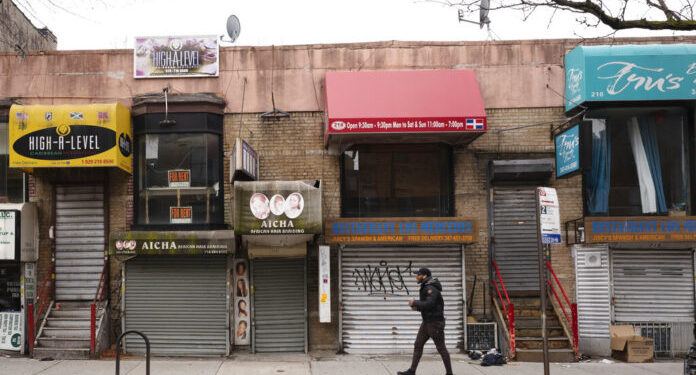 Fotografía de archivo del 8 de abril de 2020 de un peatón caminando frente a pequeños negocios que debieron cerrar sus puertas por la pandemia de coronavirus en el barrio Crown Heights de Brooklyn, en Nueva York. (AP Foto/Mark Lennihan, Archivo)