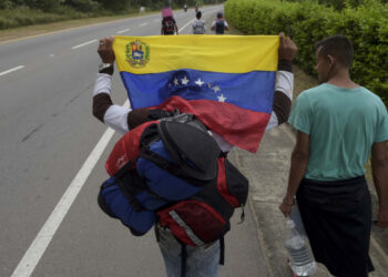 A Venezuelan migrant holding a national flag walks with other migrants on the road from Cucuta to Pamplona, in Norte de Santander Department, Colombia, on February 10, 2019. - Opposition leader Juan Guaido, recognized by some 50 countries as Venezuela's interim president, warned the military Sunday that blocking humanitarian aid from entering the country is a "crime against humanity." (Photo by Raul ARBOLEDA / AFP)