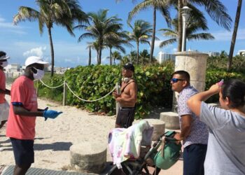 Unos jóvenes revisan las máscaras de unas personas a su llegada el 10 de junio de 2020 a la playa de Miami Beach, Florida. Foto EFE.