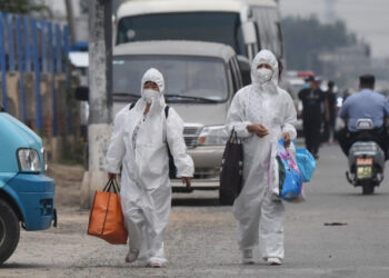 Two women wear protective suits as they walk on a street near the closed Xinfadi market in Beijing on June 13, 2020. - Eleven residential estates in south Beijing have been locked down due to a fresh cluster of coronavirus cases linked to the Xinfadi meat market, officials said on June 13. (Photo by GREG BAKER / AFP)