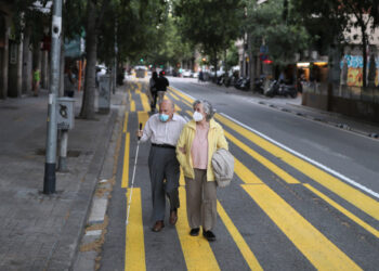 Un matrimonio de ancianos con mascarillas pasea por una franja de color pintada para el uso de peatones a fin de mantener el distanciamiento social, durante el brote de la enfermedad del nuevo coronavirus (COVID-19) en Barcelona, España, el 11 de mayo de 2020. REUTERS/Nacho Doce