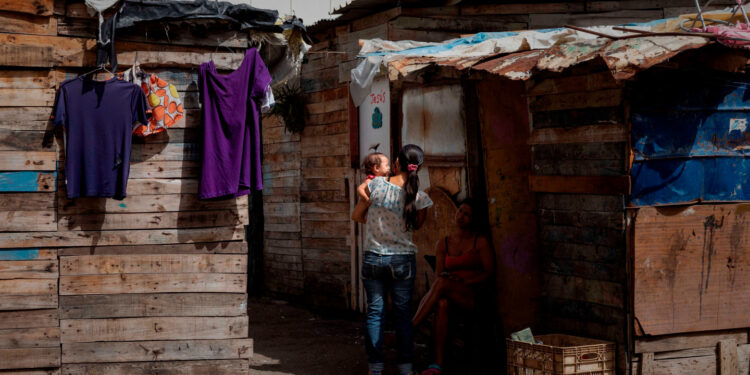 ACOMPAÑA CRÓNICA VENEZUELA CRISIS***AME2816. CARACAS (VENEZUELA), 16/07/2020.- Fotografía fechada el 11 de julio de 2020 de Thaís Pérez, de 39 años, carga a su hija de siete meses mientras habla con una vecina frente a su vivienda improvisada en un terreno ocupado en Caracas (Venezuela). De acuerdo con la Encuesta de Condiciones de Vida (Encovi), en Venezuela casi uno de cada diez niños menores de cinco años -unos 166.000- padece algún tipo de desnutrición si se atiende a la relación entre su peso y edad. Y si la relación es entre talla y edad, el dato salta a tres de cada diez, es decir, 639.000 infantes. El número no extraña a los venezolanos, que atraviesan hace más de un lustro por la peor crisis que ha visto el país en su historia moderna. EFE/ Rayner Peña R.