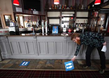 Owner Are Kjetil Kolltveit from Norway places markers for social distancing on the front of the bar at the Chandos Arms pub in London, Wednesday, July 1, 2020. Asking people in English pubs to keep their distance is going to be tough after they’ve had a few of their favorite tipples. Pub managers will have to be resourceful come Saturday, July 4, 2020, when they and other parts of the hospitality industry in England open their doors to customers for the first time since March 20, provided they meet COVID safety requirements. (AP Photo/Frank Augstein)