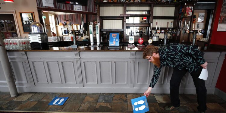 Owner Are Kjetil Kolltveit from Norway places markers for social distancing on the front of the bar at the Chandos Arms pub in London, Wednesday, July 1, 2020. Asking people in English pubs to keep their distance is going to be tough after they’ve had a few of their favorite tipples. Pub managers will have to be resourceful come Saturday, July 4, 2020, when they and other parts of the hospitality industry in England open their doors to customers for the first time since March 20, provided they meet COVID safety requirements. (AP Photo/Frank Augstein)
