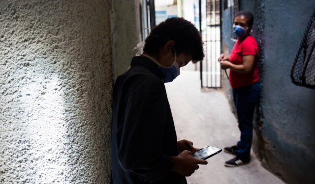 Jhonatan Figueroa, 14, uses his cellphone, connected to a neighbour's wifi signal, outside his home, as his mother Viviana Rodriguez looks at him, at the Bello Campo neighborhood in Chacao, Caracas, on October 6, 2020, amid the new coronavirus pandemic. - With students that have to catch internet in the streets and teachers who earn 2,5 US dollars a month, classes start up again in Venezuela. (Photo by Cristian Hernandez / AFP)