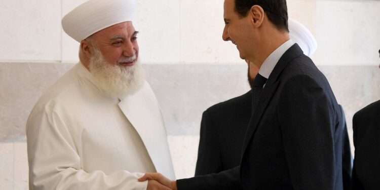 (FILES) In this file handout photo released by the official Syrian Arab News Agency (SANA) on May 20, 2019 shows President Bashar al-Assad shaking hands with cleric Adnan al-Afiyuni (L), director of Sham Islamic centre, during the inauguration of the centre that is dedicated to counter terrorism and extremism, in the Syrian capital Damascus. - Cleric Adnan al-Afiyuni was killed on October 22, 2020 after a bomb was planted in his car in the city of Qudsaya, northwest of Damascus, according to SANA. (Photo by - / SANA / AFP) / == RESTRICTED TO EDITORIAL USE - MANDATORY CREDIT "AFP PHOTO / HO / SANA" - NO MARKETING NO ADVERTISING CAMPAIGNS - DISTRIBUTED AS A SERVICE TO CLIENTS ==