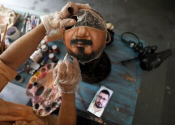 El artista plástico Jorge Silva Roriz pinta una máscara protectora personalizada mirando la foto del hombre en su teléfono celular, en medio del brote de la enfermedad del coronavirus (COVID-19), en su casa en Río de Janeiro, Brasil, 10 de noviembre de 2020. REUTERS/Pilar Olivares
