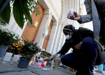 A woman lights a candle in front of the Notre-Dame de l'Assomption Basilica in Nice on October 30, 2020 during a tribute to the victims killed by a knife attacker the day before. - A 47-year-old man believed to have been in contact with the suspected knifeman who killed three at a church in Nice has been detained for questioning, a judicial source said on October 30, 2020. The man was detained late Thursday after the attack at the city's Notre-Dame basilica by a 21-year-old Tunisian who arrived in France on October 9. (Photo by Valery HACHE / AFP)