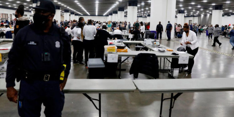 A Detroit Police officer stands guard as Detroit election workers work on counting absentee ballots for the 2020 general election at TCF Center on November 4, 2020 in Detroit, Michigan. - President Donald Trump and Democratic challenger Joe Biden are battling it out for the White House, with polls closed across the United States -- and the American people waiting for results in key battlegrounds still up for grabs. (Photo by JEFF KOWALSKY / AFP) (Photo by JEFF KOWALSKY/AFP via Getty Images)