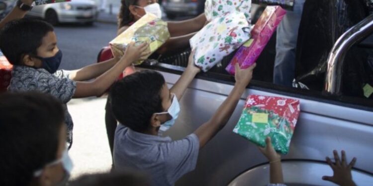 Los niños reciben regalos de Navidad donados por el grupo de voluntarios “Un Juguete, Una Buena Noticia” desde la parte trasera de una camioneta en Caracas, Venezuela, el viernes 18 de diciembre de 2020. (AP Foto/Ariana Cubillos).
